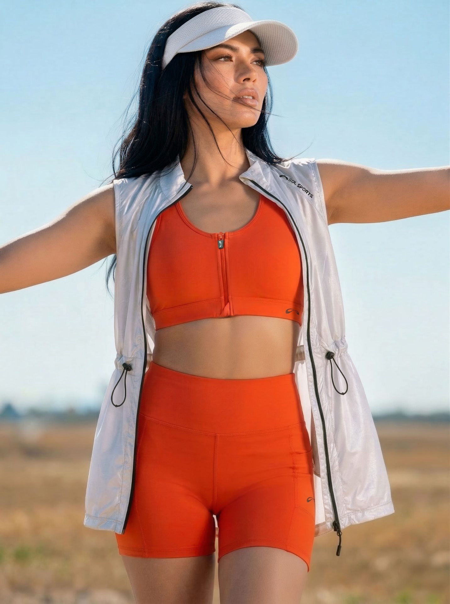 Modelo vestindo top e shorts laranja SOL Sports com colete branco, coleção CONEXÕES Verão 2027